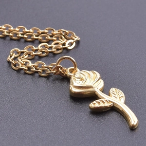 Macro shot of detailed golden rose pendant with delicate chain on dark background