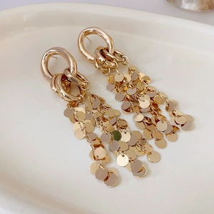 Macro view of gold flower tassel earrings with interlocking rings on a ceramic tray