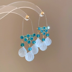 Detail of tassel earrings with blue crystals and white petal pendants on a display