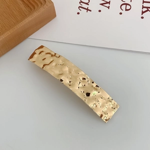 Close-up of golden geometric rectangular hair clip with hammered metal texture design