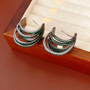 Detail of gunmetal multi-layer C-shaped earrings with green zircon in a wooden box