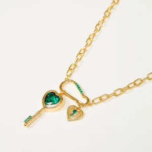 Golden necklace with emerald heart key pendant and zircon inlay on a light background