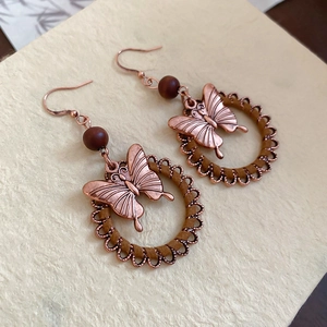 Macro view of vintage bronze butterfly earrings with wooden beads and leather cords