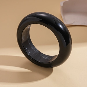 Detail of a thick black resin bangle featuring a white marble texture on a beige background