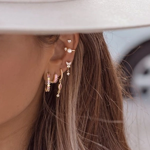 Macro shot of gold-plated earring set featuring colorful zircons and pearls on model ear