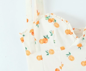 Detailed close-up of lace trim and vibrant orange fruit print on white dress fabric