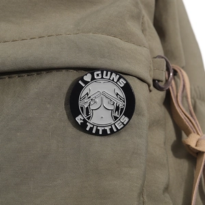 Runde schwarze Emaille-Brosche mit Grafik-Design auf einem beigen Canvas-Rucksack