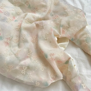Detail of embroidered tulle fabric with soft floral patterns and bowknot stitching