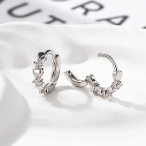 Silberne Huggie-Ohrringe mit Herz und Zirkon auf weißem Seidenstoff elegant präsentiert
