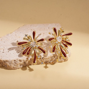 Close-up of golden fireworks earrings with red enamel and white zircon on stone