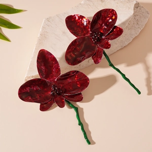 Detailed shot of red enamel flower earrings with green stems on a decorative stone base
