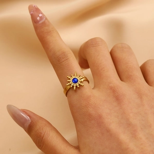 Detail van 18K goudkleurige zonnestraal ring met blauwe edelsteen op zijden stof