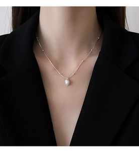 Close-up of a silver beaded chain with a baroque pearl pendant worn on a black blazer