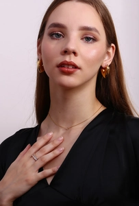 Model wearing gold heart earrings and minimalist zircon necklace on a grey background