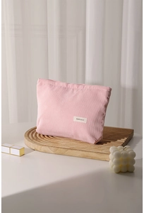 Pink corduroy makeup bag on wood tray with soft lighting for travel storage