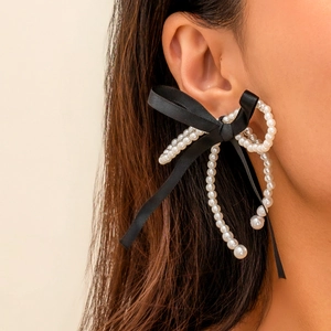 Close-up of elegant bow earrings featuring white faux pearls and black ribbon tassels