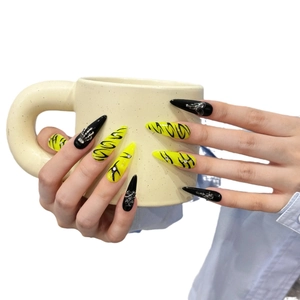 Handmade stiletto press-on nails with yellow and black gothic skull art on a ceramic cup
