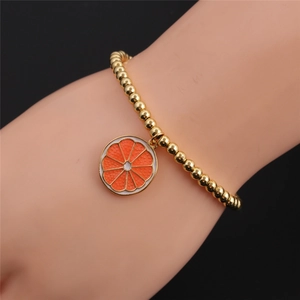 Gold beaded bracelet with orange slice pendant worn by model on dark background
