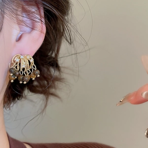 Detail of zircon fireworks tiger eye stone tassel earrings worn by a model in soft light