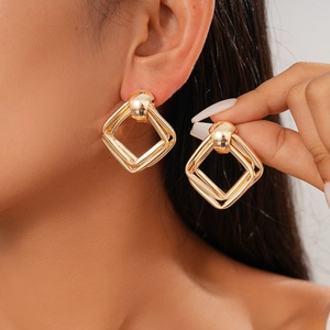 Modern gold geometric square drop earrings worn by a model against a white wall background