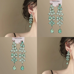 Macro shot of long layered silver earrings with green water-drop pendants on card