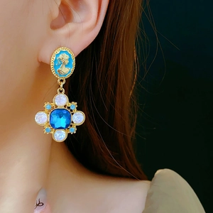Close-up of vintage gold earrings with blue cameo portrait and crystal drop pendant