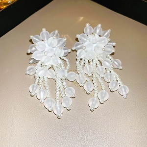 Close-up of white floral tassel earrings with matte beads and pearls on a beige background