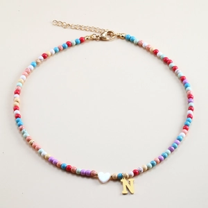 Detail of colorful beaded necklace featuring a golden N letter charm and heart pendant