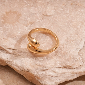 Detailed view of a gold liquid droplet shaped metal ring on a textured stone surface