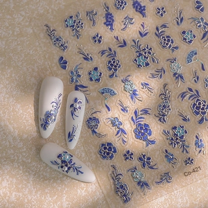 Détail de stickers à ongles fleuris bleus en relief avec motifs argentés sur faux ongles