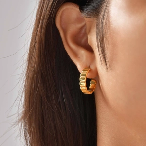 Macro detail of golden hoop earrings featuring unique textured ridges and C-shaped design