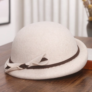 Detail of off-white wool beret with brown ribbon bow on a dark wood surface