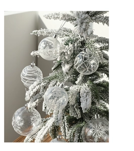 Close-up of clear Christmas ball with white snowflake patterns on a snowy pine tree