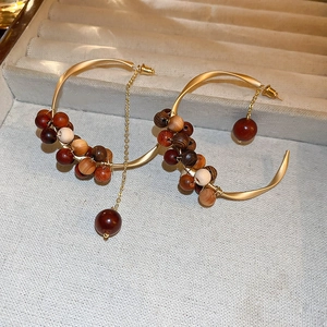 Detail of matte gold C-shaped earrings with brown leopard style wooden beads and tassels