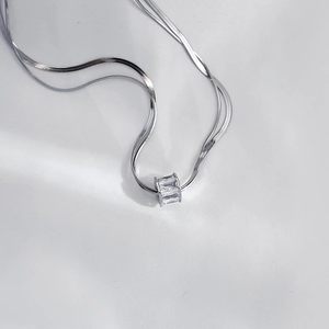 Detail shot of a double-layer silver snake chain with a rectangular zircon cylinder pendant