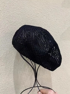 Close-up of black hollow mesh beret showing intricate knit texture on a metal stand