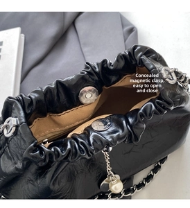 Detail of black pleated cloud bag showing magnetic closure and silver chain with pearl