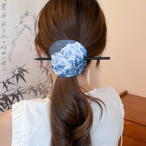 Detailansicht einer eleganten runden Haarnadel mit blauen Wellenmustern am Dutt