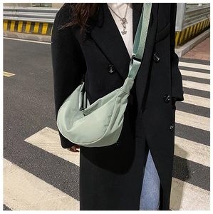 Bean green nylon half-moon crossbody bag shown in a stylish urban street setting