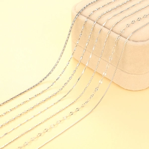 Close-up of various silver chains including snake, box, and beaded styles on yellow backdrop