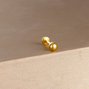 Macro shot of a polished gold ball labret piercing on a luxurious silk satin surface