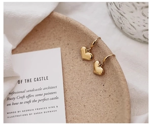 Macro shot of French vintage style golden heart drop earrings on a minimalist tray
