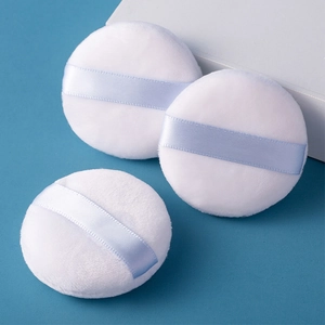 White flocking powder puffs with light blue satin ribbons on a clean blue background