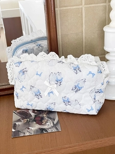 Detail of white heart-quilted makeup bag with lace trim and blue cat ribbon patterns