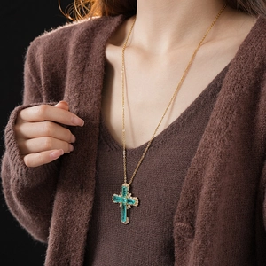 Close-up of golden cross pendant featuring emerald green stones and zircon detailing