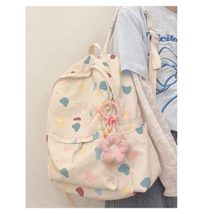 Close-up of cream canvas backpack featuring colorful cloud patterns and a pink floral charm