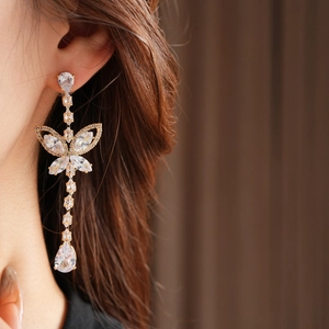 Close-up of elegant gold tassel earrings with butterfly zircon pendants on a model