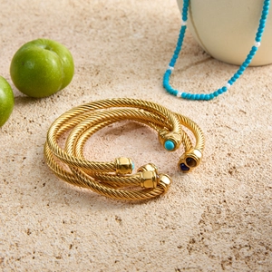 Detail of twisted cable gold bracelets with inlaid blue natural stones on a stone background