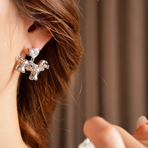 Close-up of silver dachshund dog earrings with heart zircon stone worn by a model