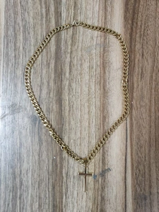 Close-up of a gold Cuban chain necklace with a minimalist cross pendant on wood surface